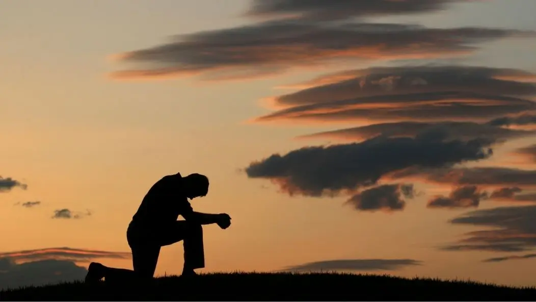 Silhouette of a man kneeling in prayer at sunset, reflecting the difference between a strong man and a godly man.